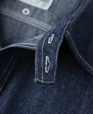 Dark blue denim workshirt cuff seam with stitched logo patch on placket