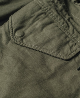 Olive field jacket pocket flap with visible stitching and button hardware