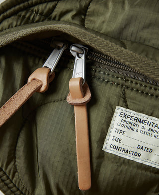 Close-up of olive bag zipper pulls with tan leather-style tabs and label tag