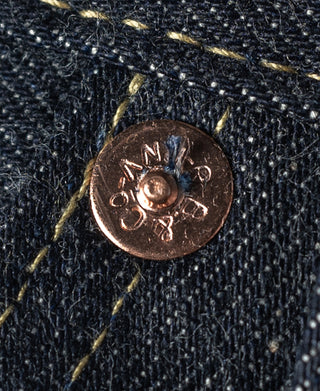 Indigo denim jeans close-up of copper-tone button on coin pocket.