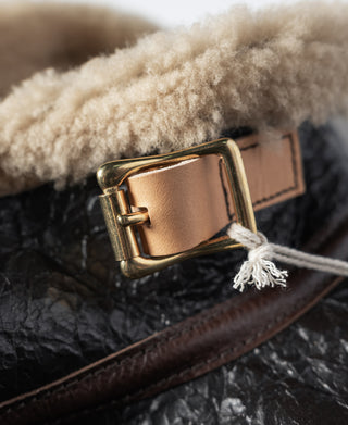 Metal buckle on flight jacket neck strap with tan shearling lining and brown leather
