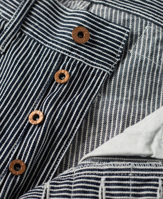 Striped carpenter pants waistband and pocket area with brown buttons and stitched panels.
