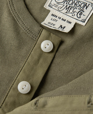 Olive henley t-shirt placket close-up with white buttons and ribbed collar texture