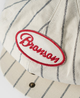 White pinstripe newsboy cap with Bronson red-and-white logo patch