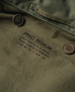 Olive field jacket label reading "SMALL REGULAR" near two button closures