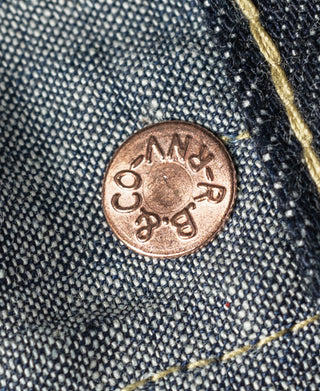 Indigo denim jeans close-up of copper-tone coin pocket button with engraved text.