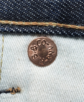 Copper-tone fabric patch on indigo denim with stamped logo