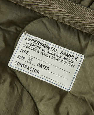 Olive jacket care label reading “EXPERIMENTAL SAMPLE” and size M