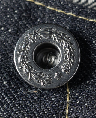 Metal button close-up on indigo denim with decorative engraved pattern