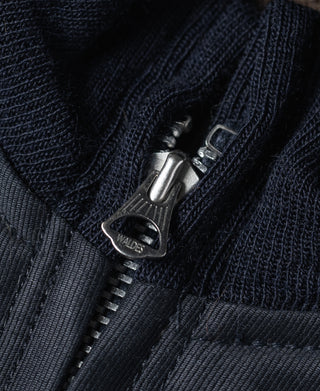 Navy deck jacket zipper close-up with metal pull and branded tab