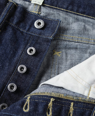 Indigo denim jeans with metal button flap and stitched coin pocket, close-up