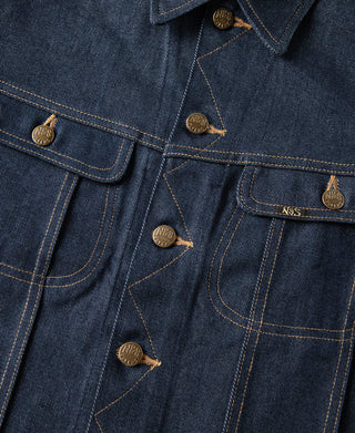 Indigo denim jacket front close-up with flap pockets, brass buttons, and stitch lines.