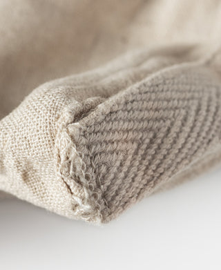 Natural linen tote bag bottom corner with textured stitching and folded edge.