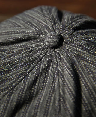 Black and gray newsboy cap crown close-up with gathered top seam.