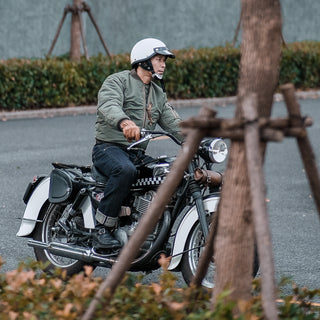 Olive MA-1 flight jacket on model seated by motorcycle, front zipper and ribbed cuffs visible