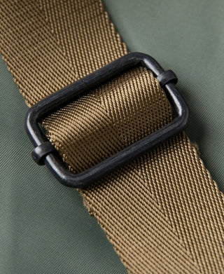 Brown canvas webbing strap with black buckle and stitched edge on sage green bag