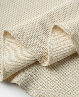 Thermal waffle-knit shirt hem and drape; light apricot/cream fabric close-up