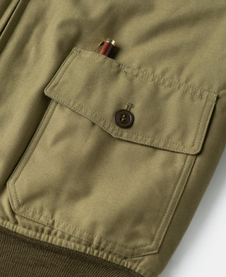 Khaki flight jacket chest pocket with button flap and top zipper seam detail.