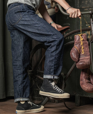 Dark indigo denim jeans with front pockets and cuffed hem, worn with sneakers