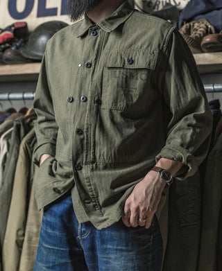 Olive utility jacket with flap chest pocket and button front, worn with jeans