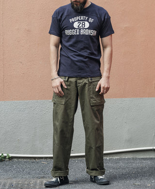 Model wearing navy crew-neck football t-shirt with “PROPERTY OF 28” “RUGGED BRONSON” graphic