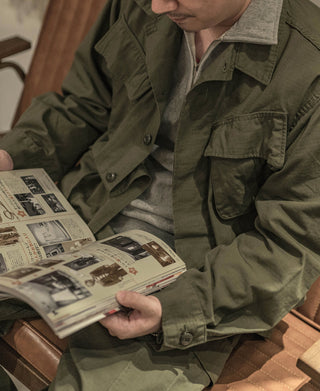 Olive fatigue jacket with flap chest pockets and button front, worn over a gray layer