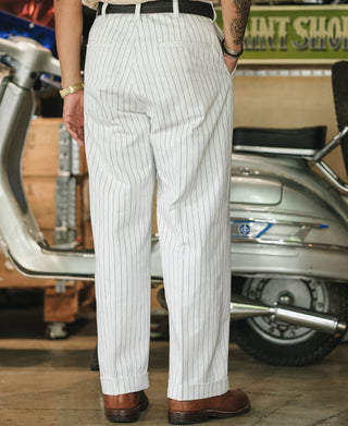 White pinstripe work pants with pleats and cuffs, worn with belt and brown shoes