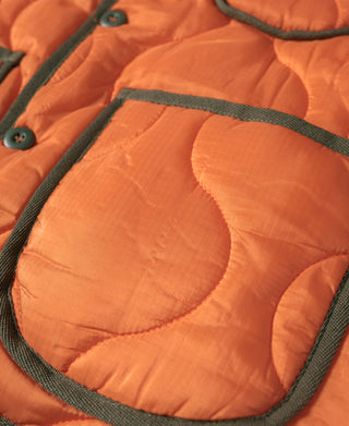 Orange quilted ripstop jacket close-up with dark-trim pocket and button-placket edge