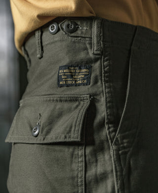Olive utility pants close-up, size label patch and buttoned pocket flap
