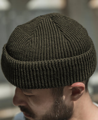 Olive knit watch cap on model, close view of ribbed fabric texture