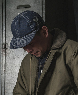 Indigo denim A-3 style cap worn, front-left view with dark emblem on side