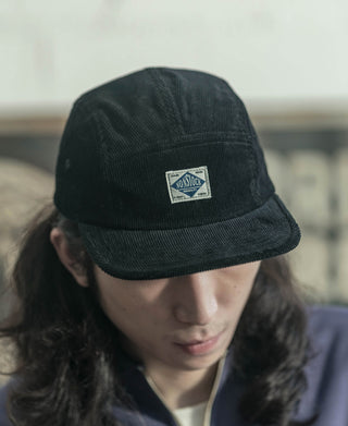 Black corduroy 5-panel cap on a person, front logo patch visible