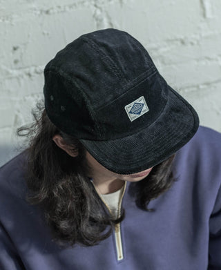 Black corduroy 5-panel cap with triangular logo patch and curved brim