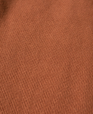 Orange cotton-terry sweatpants fabric close-up with textured knit surface