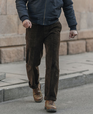Dark brown corduroy work pants with straight legs and cuffed hem, worn.