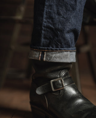 Selvedge cuff detail on dark indigo denim jeans with leather strap boot