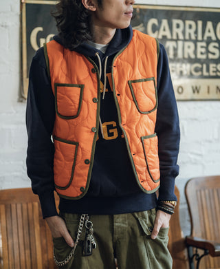 Orange padded quilted vest worn over hoodie, with button front and two chest patch pockets