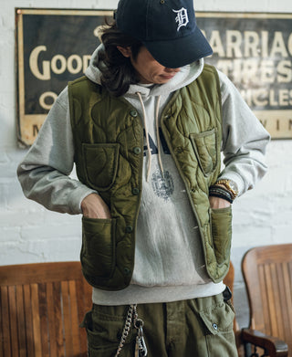 Olive quilted padded nylon vest worn over a hoodie, front pockets and snap placket visible