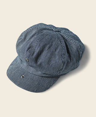 Striped denim newsboy cap with dark blue brim, white pinstripes, and side snap detail.