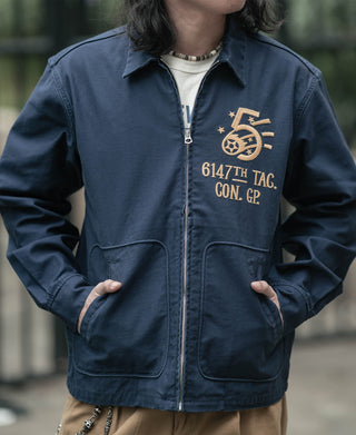Navy tour jacket with front zip and two chest pockets, featuring embroidered badge graphic