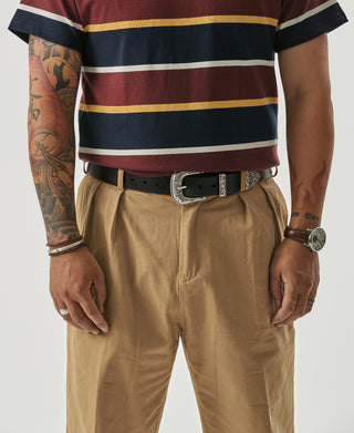 Yellow chino trousers with pleats, belt loops, and a dark patterned leather belt