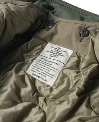 Olive quilted jacket liner close-up: snap buttons and care label at chest