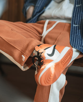 Orange sweatpants detail with cuff hem and side stripe, shown with sneakers