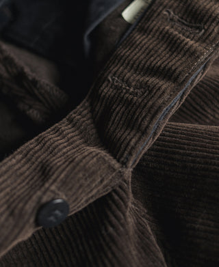 Dark brown corduroy fabric with visible seam and metal button detail.