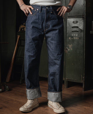 Dark indigo denim jeans with button fly, belt loops, and light selvedge cuff at ankles