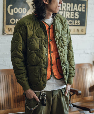 Olive quilted padded jacket with button front and patch pockets over orange shirt
