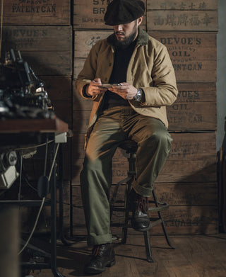 Olive M-43 field trousers on person, sitting pose with straight legs and dark boots