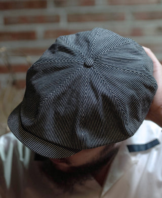 Striped denim newsboy cap, dark blue with white zigzag pinstripes and structured brim.