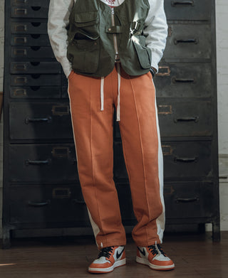 Orange straight-leg sweatpants with drawstring and logo at hip, worn with sneakers
