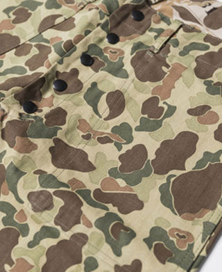 Reversible camo pants fabric close-up with stitched pocket edge and dark buttons